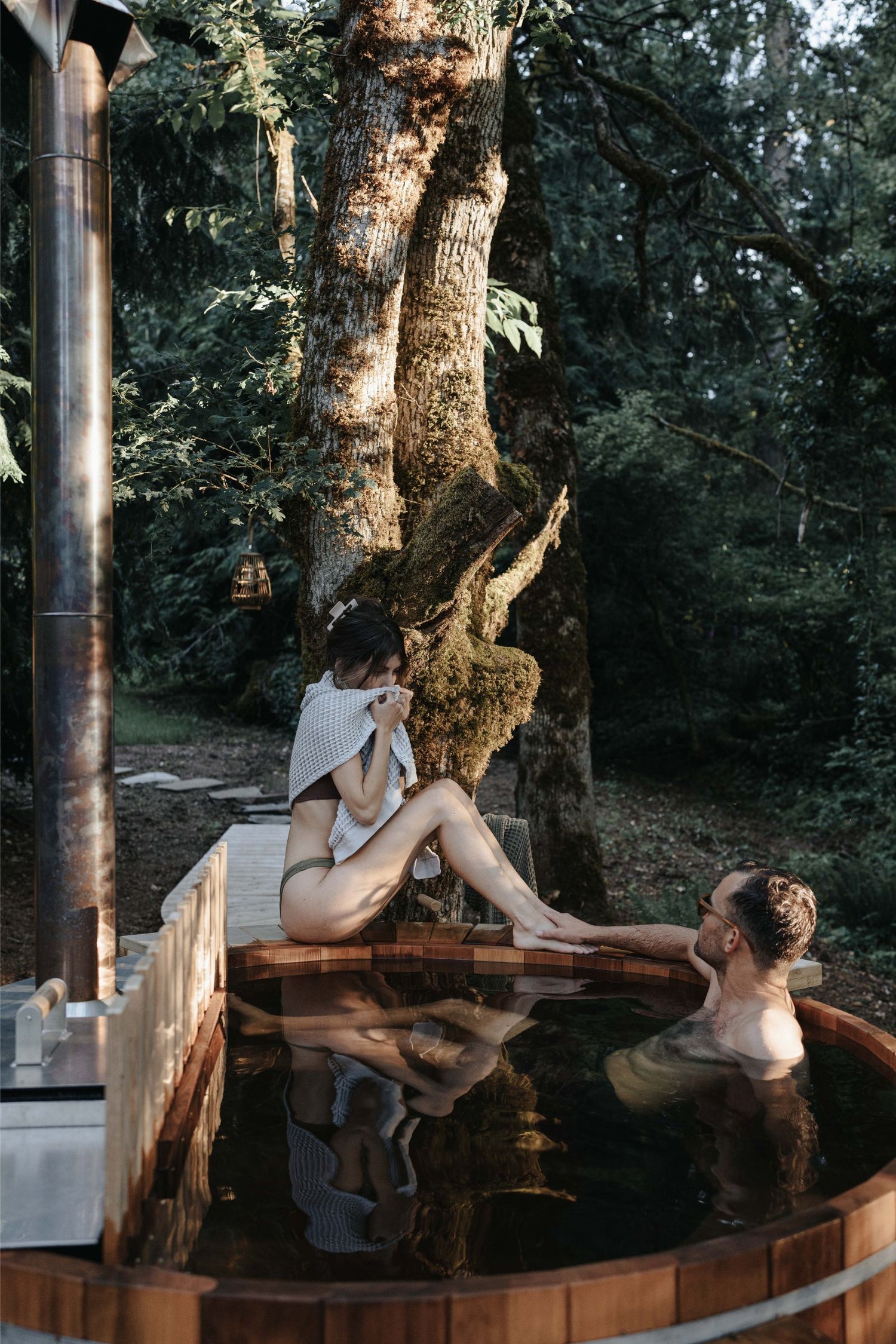 Two people in an outdoor hot tub surrounded by trees
