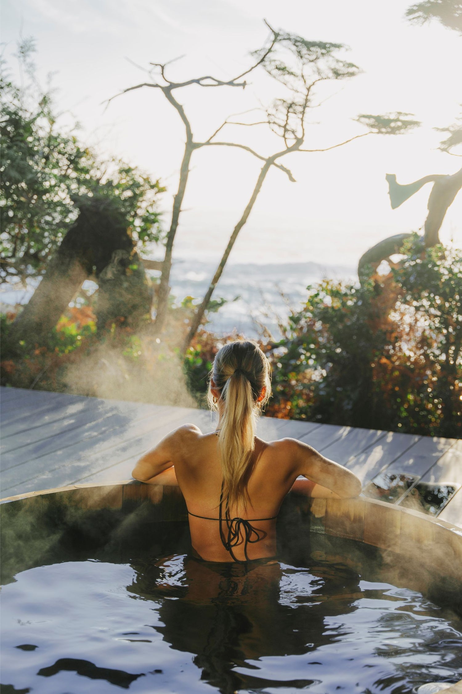 Woman sitting in a hot tub with a scenic view of trees and mountains.