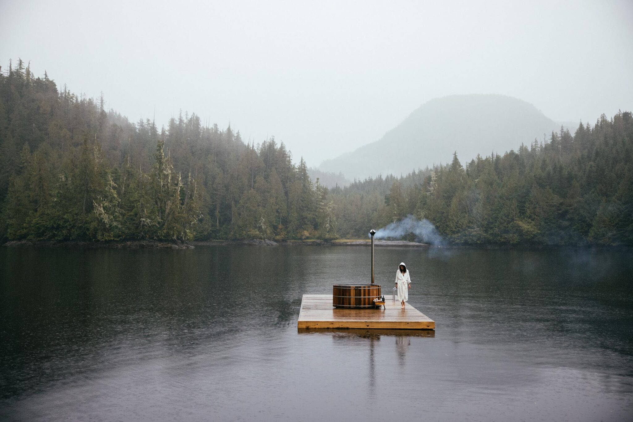 Cedar hot tub on a floating dock at Nimmo Bay Resort, surrounded by misty rainforest and calm waters.